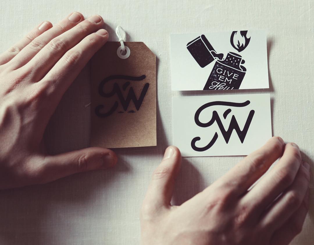Hands holding small paper tags with black lettering on a light background
