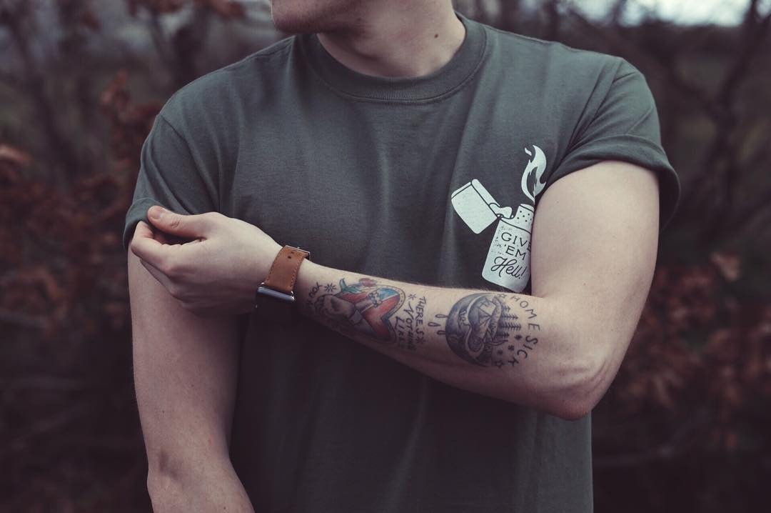 Olive green organic cotton t-shirt with white lighter flame graphic on chest, worn with sleeve rolled up.